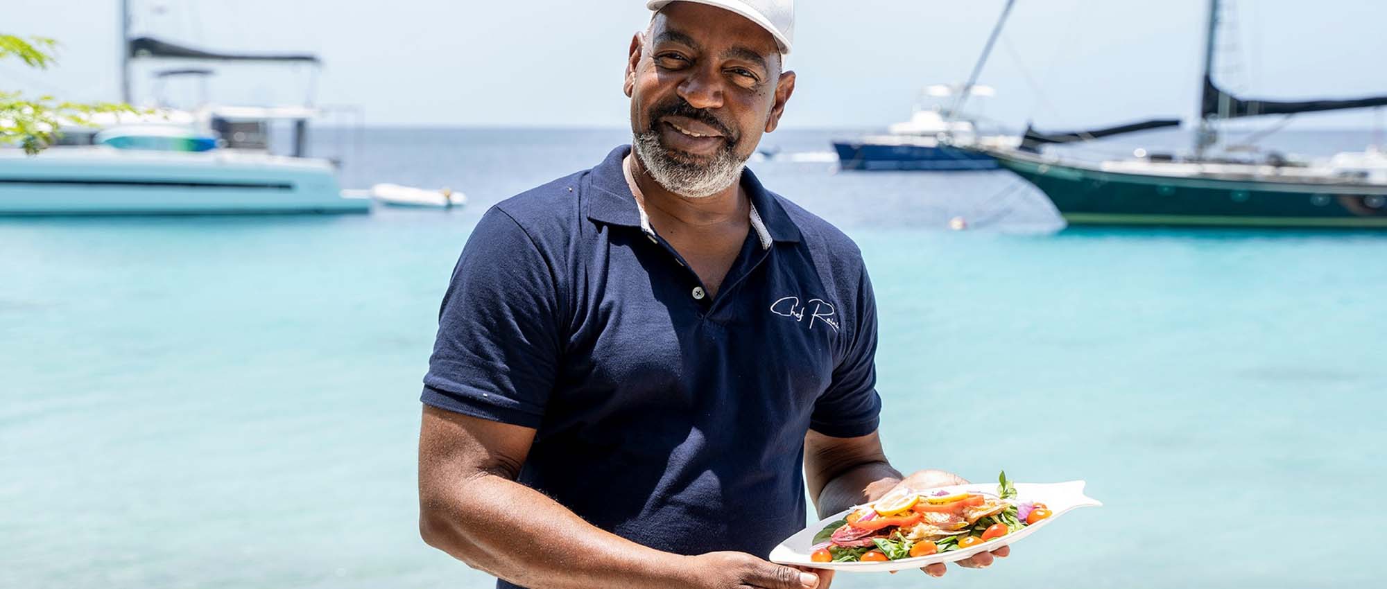 Man holding a plate of food with the ocean in the background