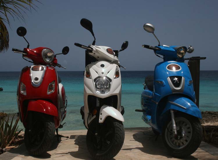 Red, white, and blue scooters lined up by the ocean