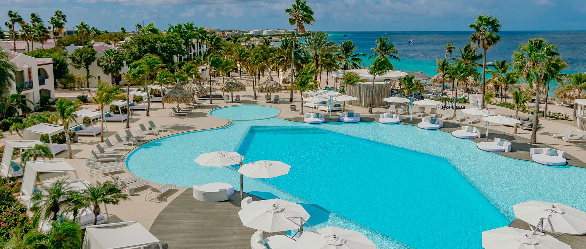 Aerial view of outdoor pool area overlooking the ocean surrounded by palm trees and cabanas