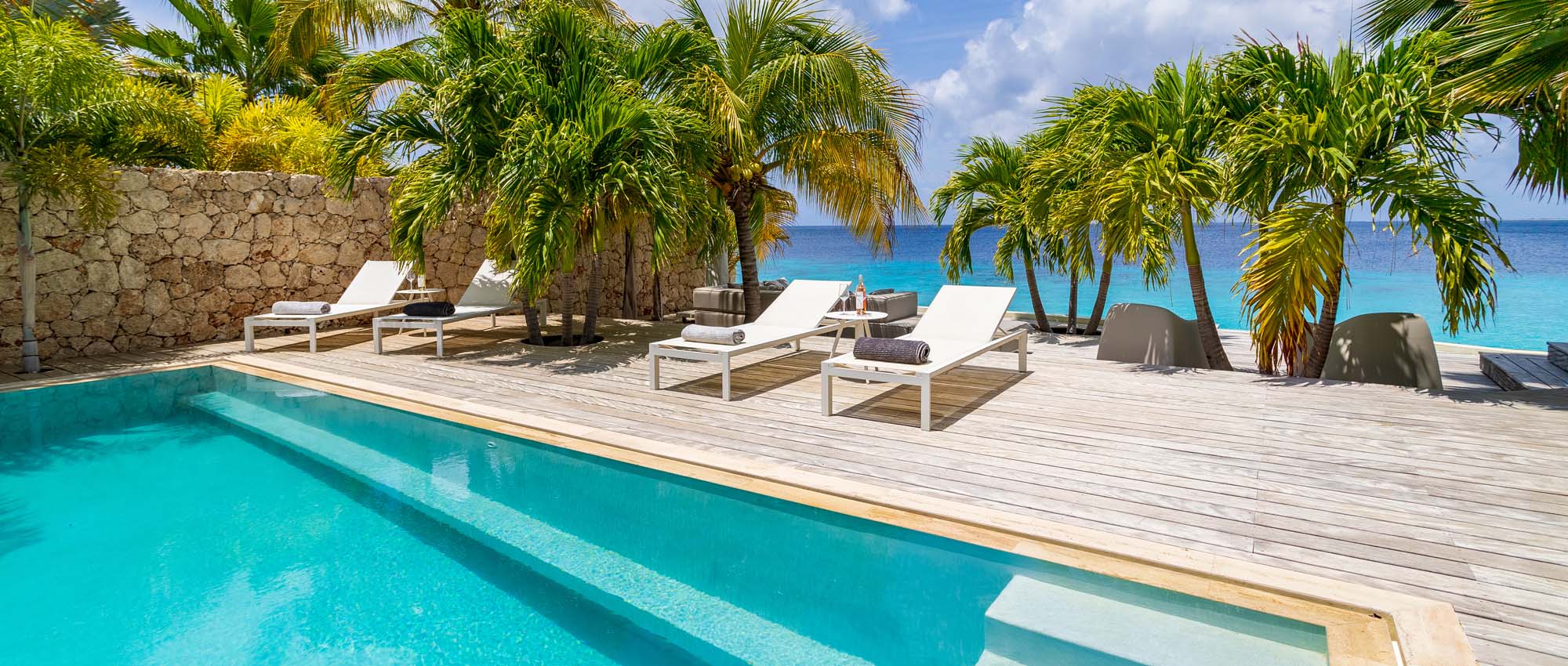 Outdoor pool area with sun lounge chairs and palm trees by the ocean