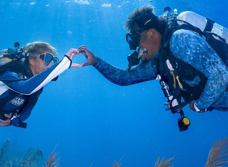 Twee duikers maken een hart met hun handen onder water